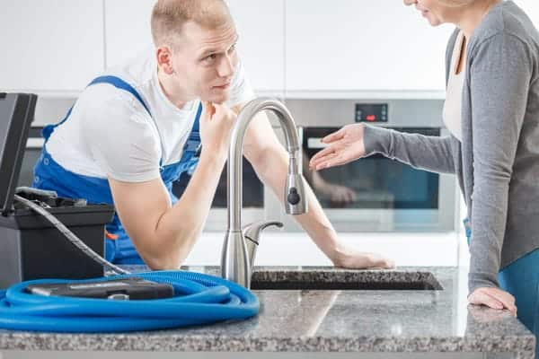 Plumber consulting with customer about dripping sink faucet next to his toolbox.