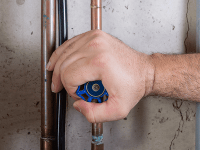 A hand turns a water shut off valve.