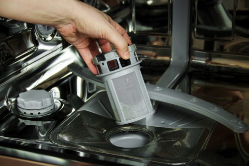 A man removes the filter from the bottom of his dishwasher.
