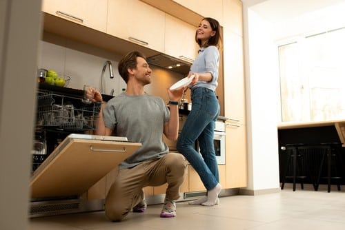 A young couple places their dishes into their dishwasher.