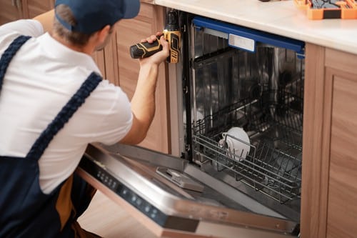 A plumber repairs a dishwasher.