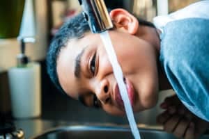 A child drinks softened water directly from the kitchen faucet.