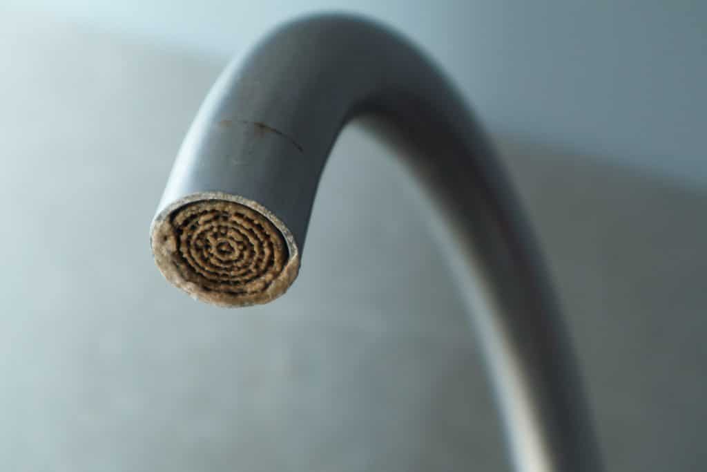 Hard water deposits on a dirty faucet aerator with limescale, a calcified shower water tap, and a heavily calcified kitchen faucet.