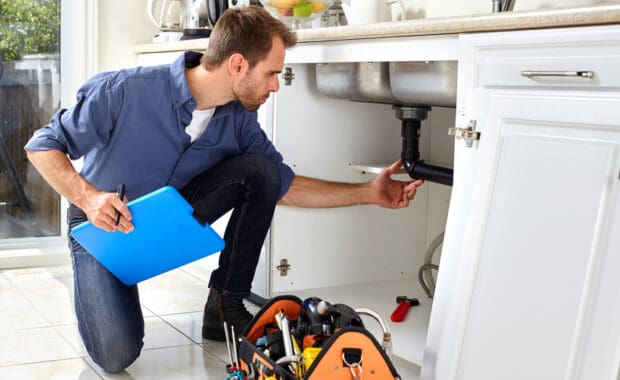 A licensed plumber inspects the pipes beneath a kitchen sink.