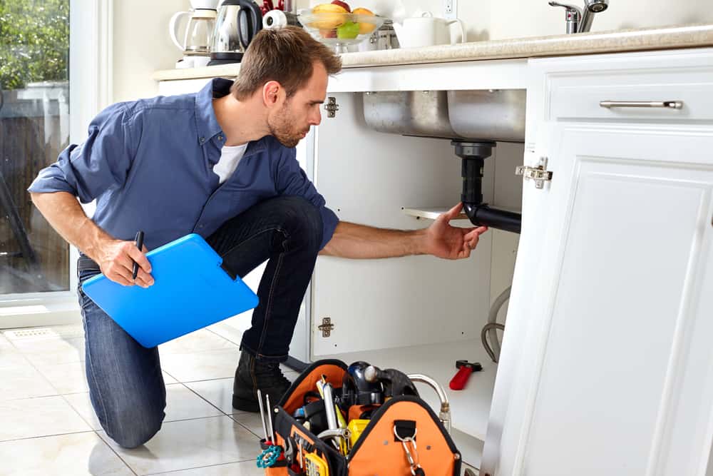 A licensed plumber inspects the pipes beneath a kitchen sink.