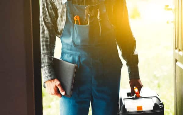 Plumber outfitted with tools and documentation stands in doorway