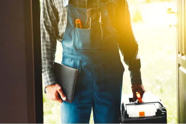 Plumber outfitted with tools and documentation stands in doorway