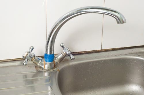 An old kitchen faucet with rust and tape holding it together.