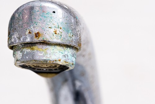 Close up of a kitchen faucet spout with mineral build up.