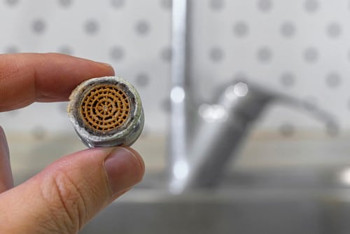 Person holding a corroded and blocked aerator from a kitchen sink.
