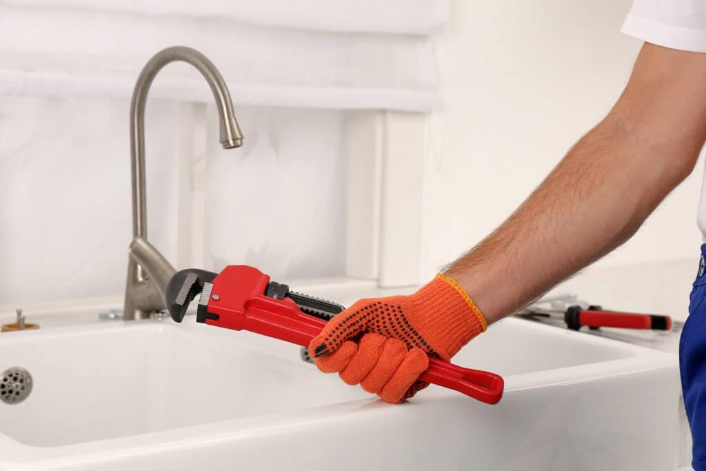 A man with a pipe wrench near the kitchen sink, installing a water tap according to Texas plumbing code.