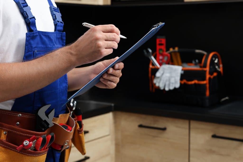 Professional plumber with a clipboard and tool belt indoors, checking pipes.