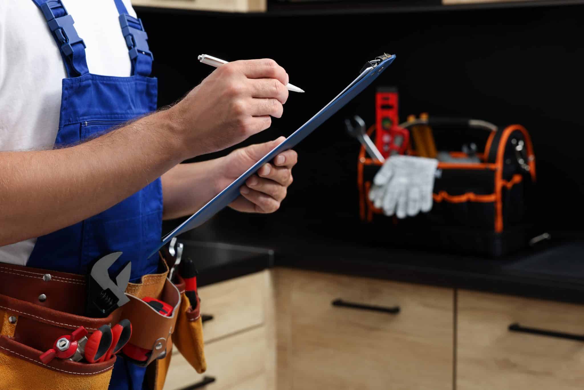 Professional plumber with a clipboard and tool belt indoors, checking pipes.
