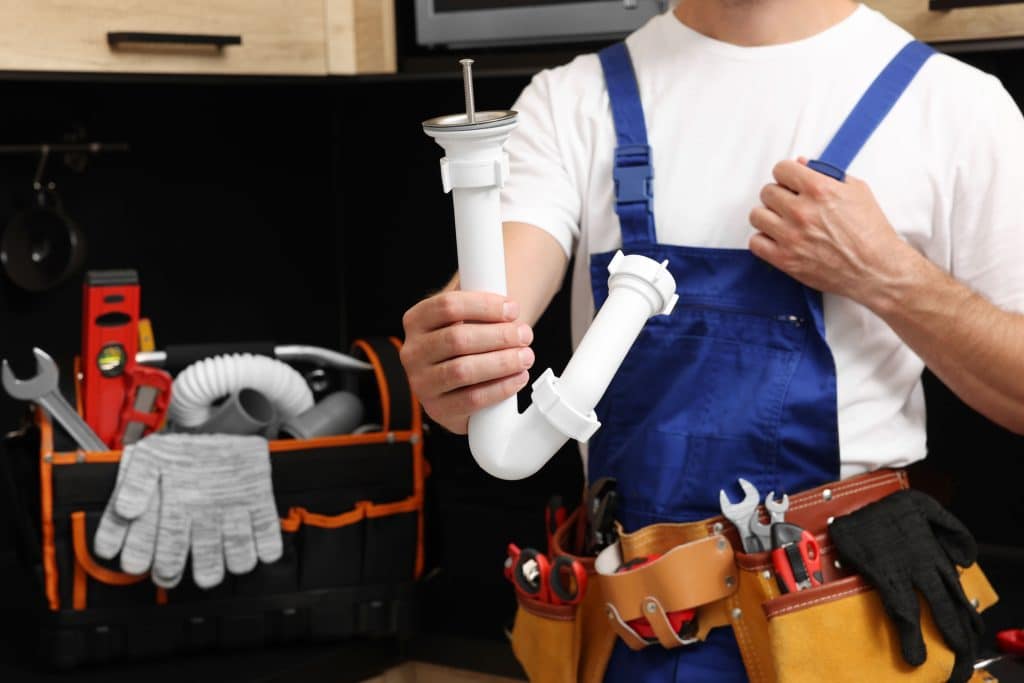 Professional plumber with corrugated pipes and a tool belt indoors.