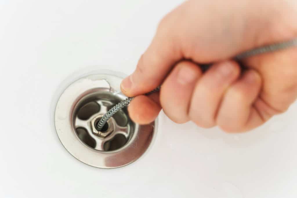 The plumber is using a drain snake to unclog the bathtub. Drain Cleaning by Benjamin Franklin Plumbing of Dallas, TX