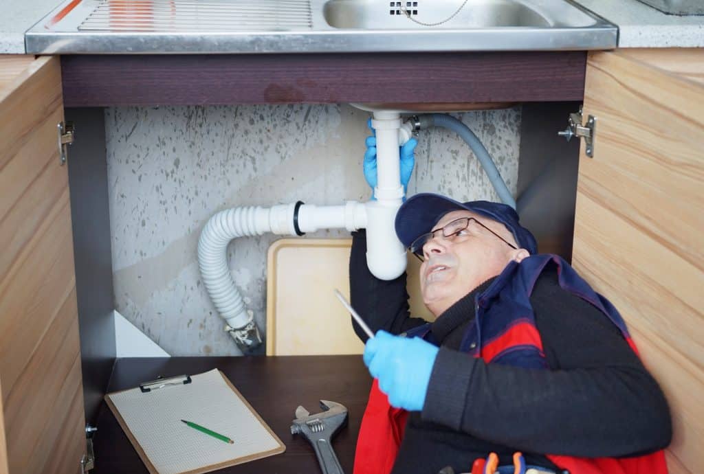 A plumber looking for hidden leaks under the sink.