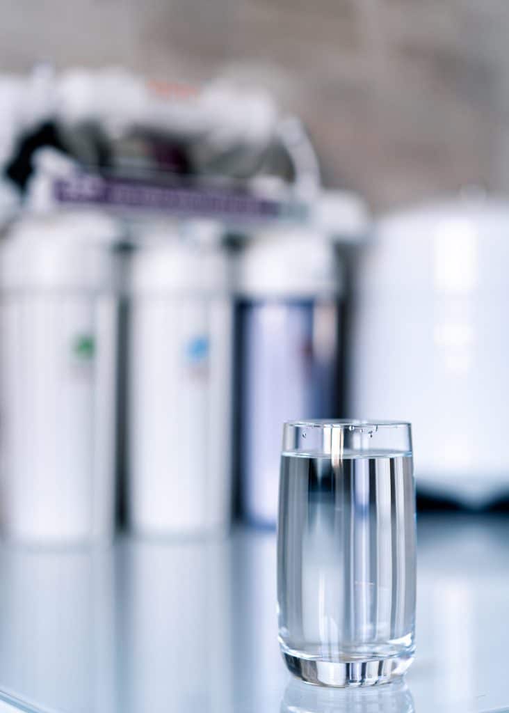 A glass of clean water and water filtration systems on a blurred background.