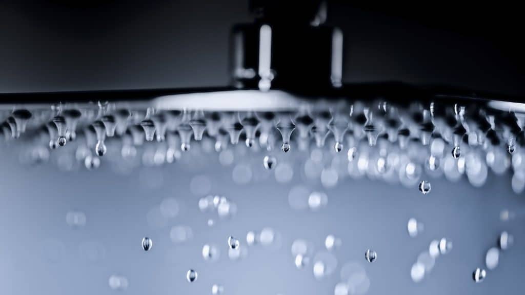 Close-up of low water pressure flowing from a showerhead in a bathroom.