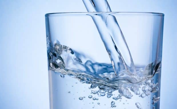 Close-up of pouring water quality into a glass on a blue background.