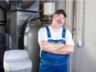 A plumbing technician stands next to a home water softener.