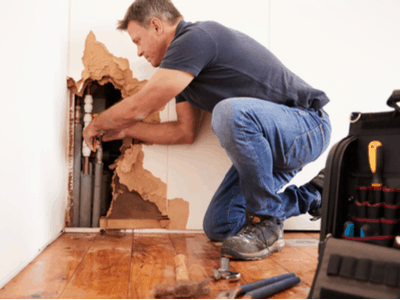 A plumber fixes pipes behind a water damaged wall.