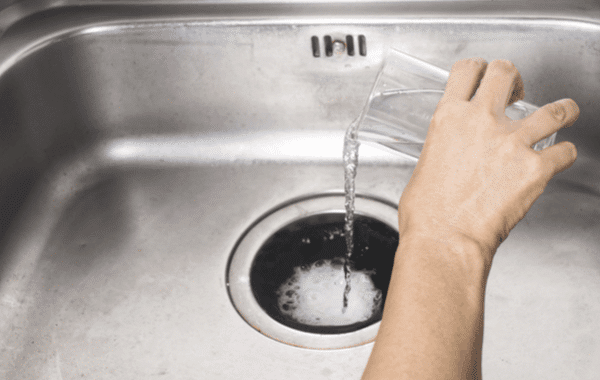 Person pouring a combination of hot water, baking soda, and vinegar into kitchen sink to clear clog