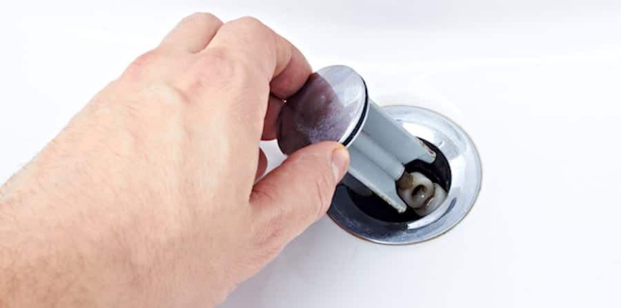Hand removing a drain plug from a sink