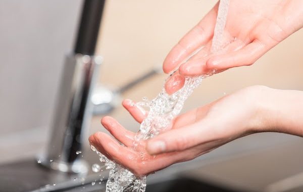 Person washing their hands at a kitchen sink. How to save money on your water bill during the coronavirus outbreak